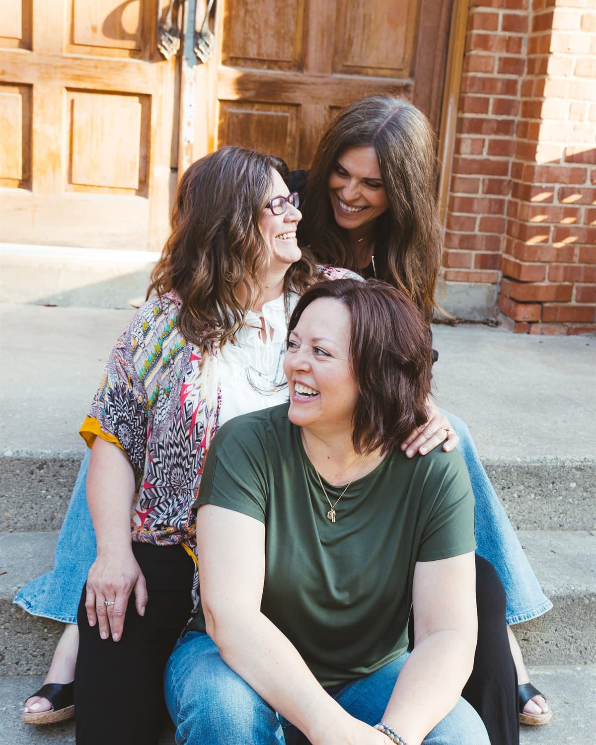 Kelly, Deena and Krista sitting together on the steps outside the venue, laughing.